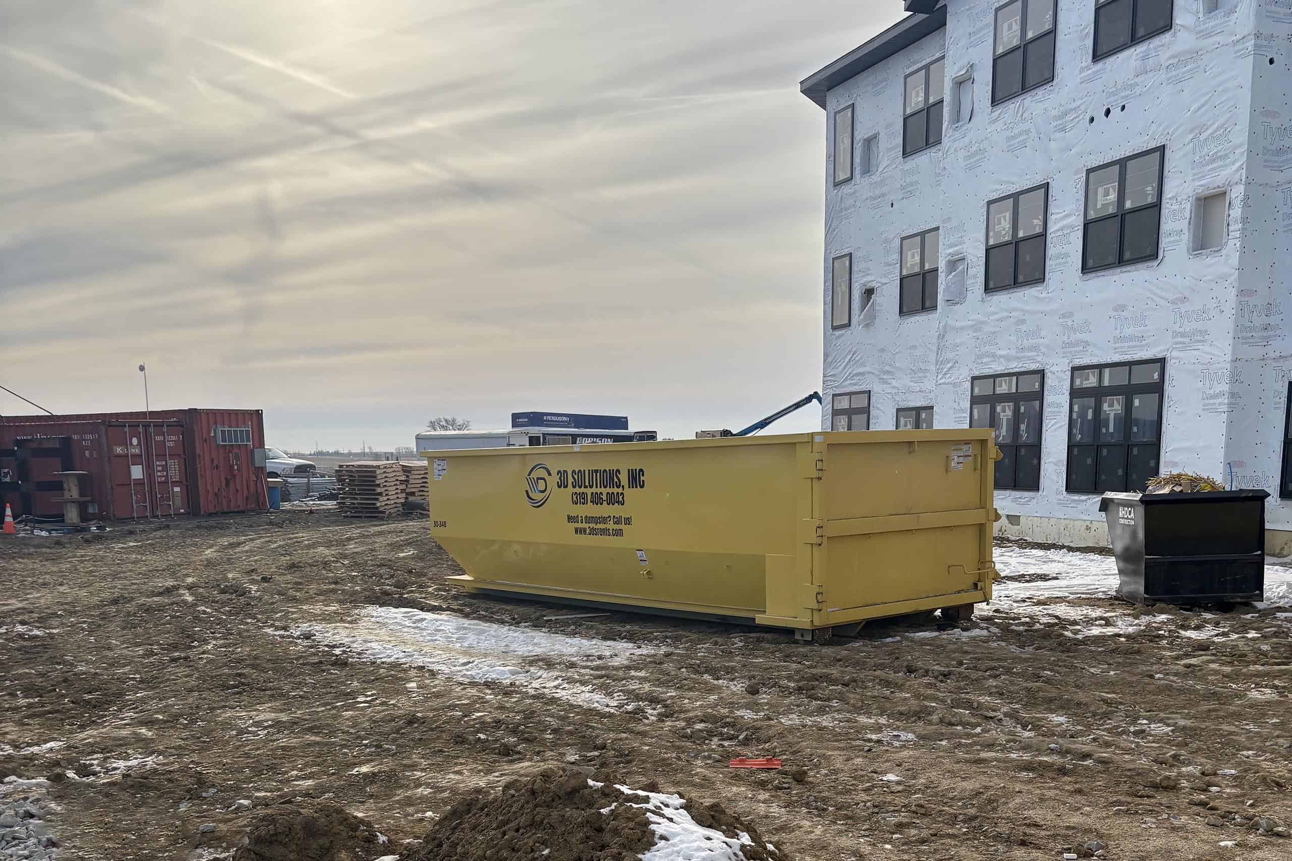 Construction site with a yellow dumpster and a partially built multi-story building.